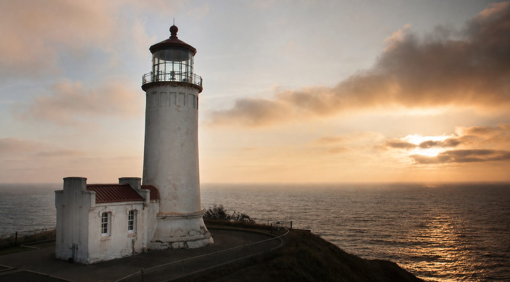 A lighthouse on the coastline with a setting sun